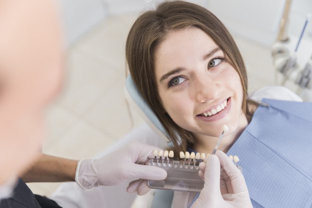 doctor choosing color tone from shade guide smiling female patient's teeth