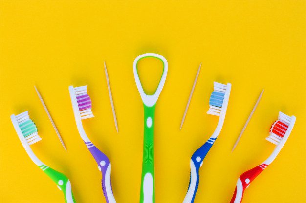 toothbrushes-toothpick-tongue-scraper-yellow-background-top